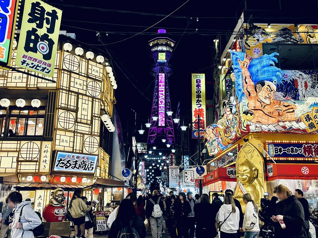 Tsutenkaku Tower rises above the illuminated streets and restaurant signs of Shinsekai, Osaka.