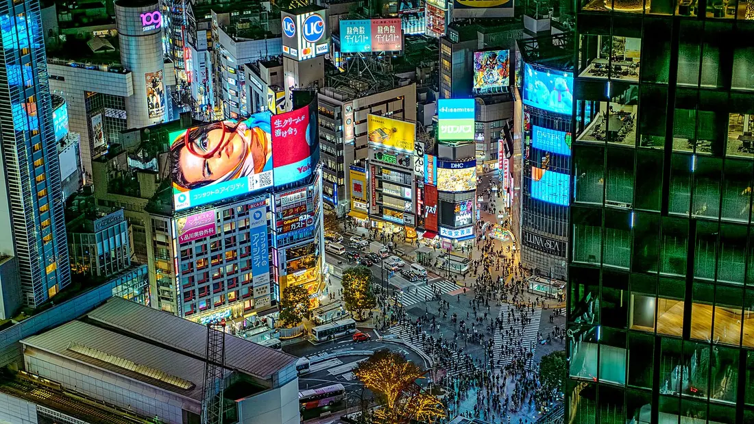 An elevated nighttime view of the pedestrian crossing and illuminated buildings in Shibuya, Tokyo.